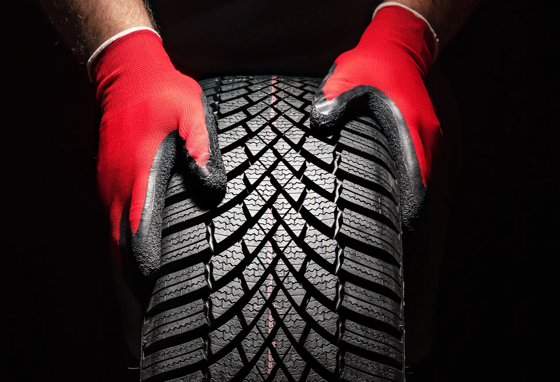 KFZ Mechaniker hält einen Reifen mit roten Handschuhen Nahaufnahme